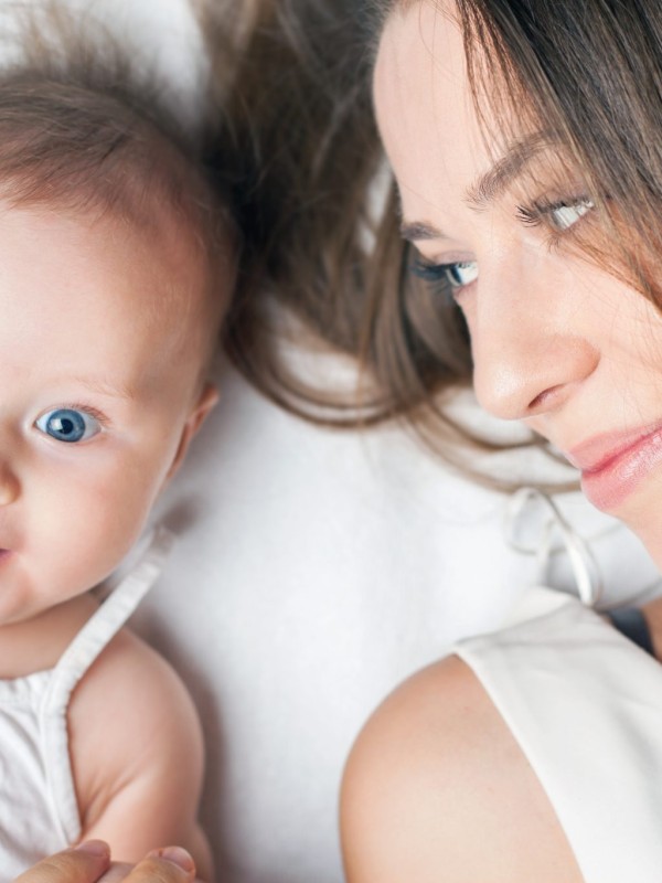Happy baby girl lying near her mother on a white bed. Newborn looking at the camera and smiling. Mothercare is most important in baby life