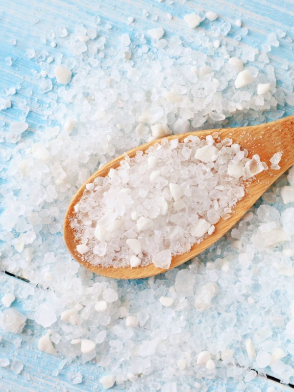 Sea salt grind on wooden light blue shabby table wooden spoon. Kitchen and cosmetic healthy usage.