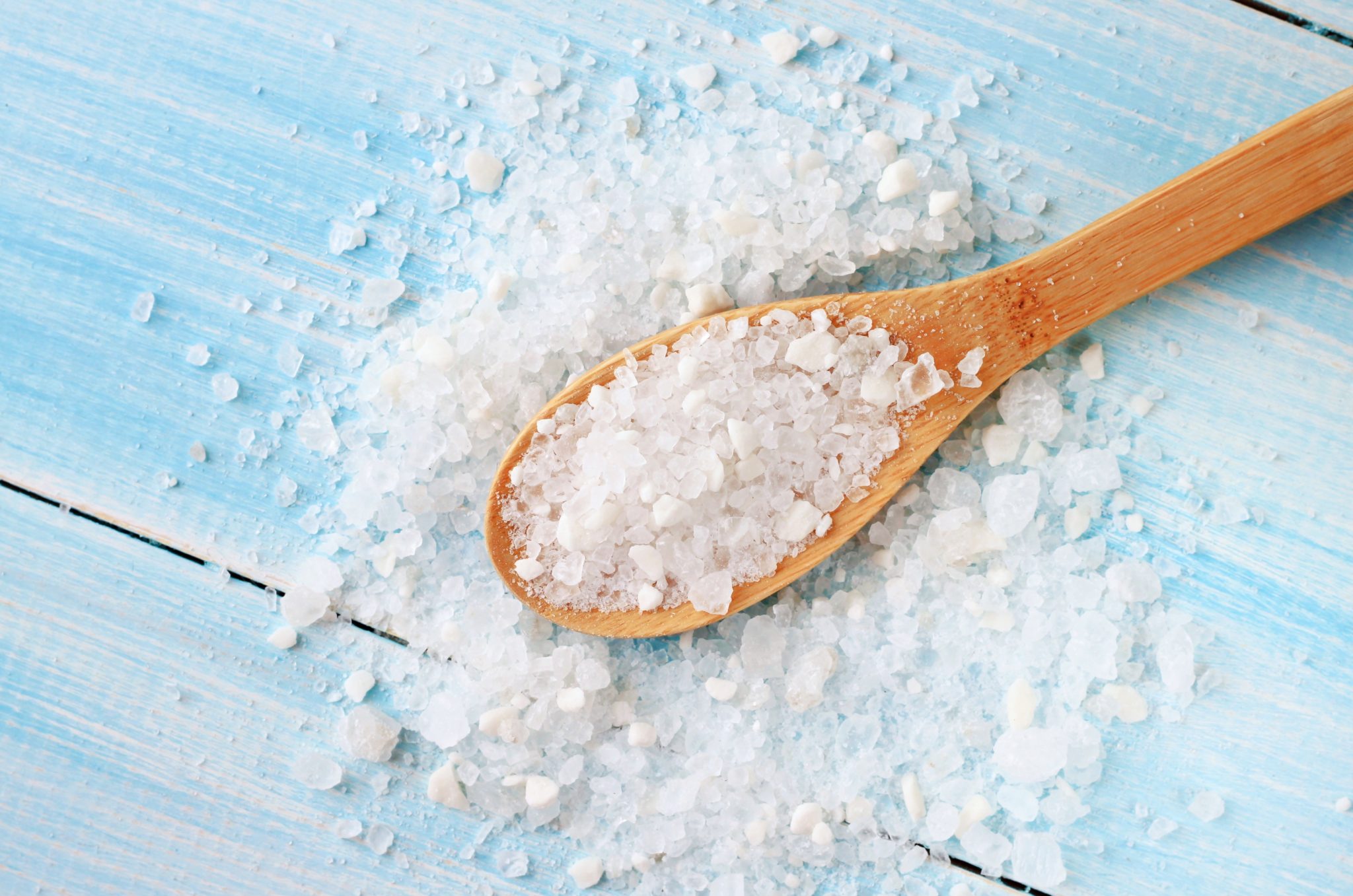 Sea salt grind on wooden light blue shabby table wooden spoon. Kitchen and cosmetic healthy usage.