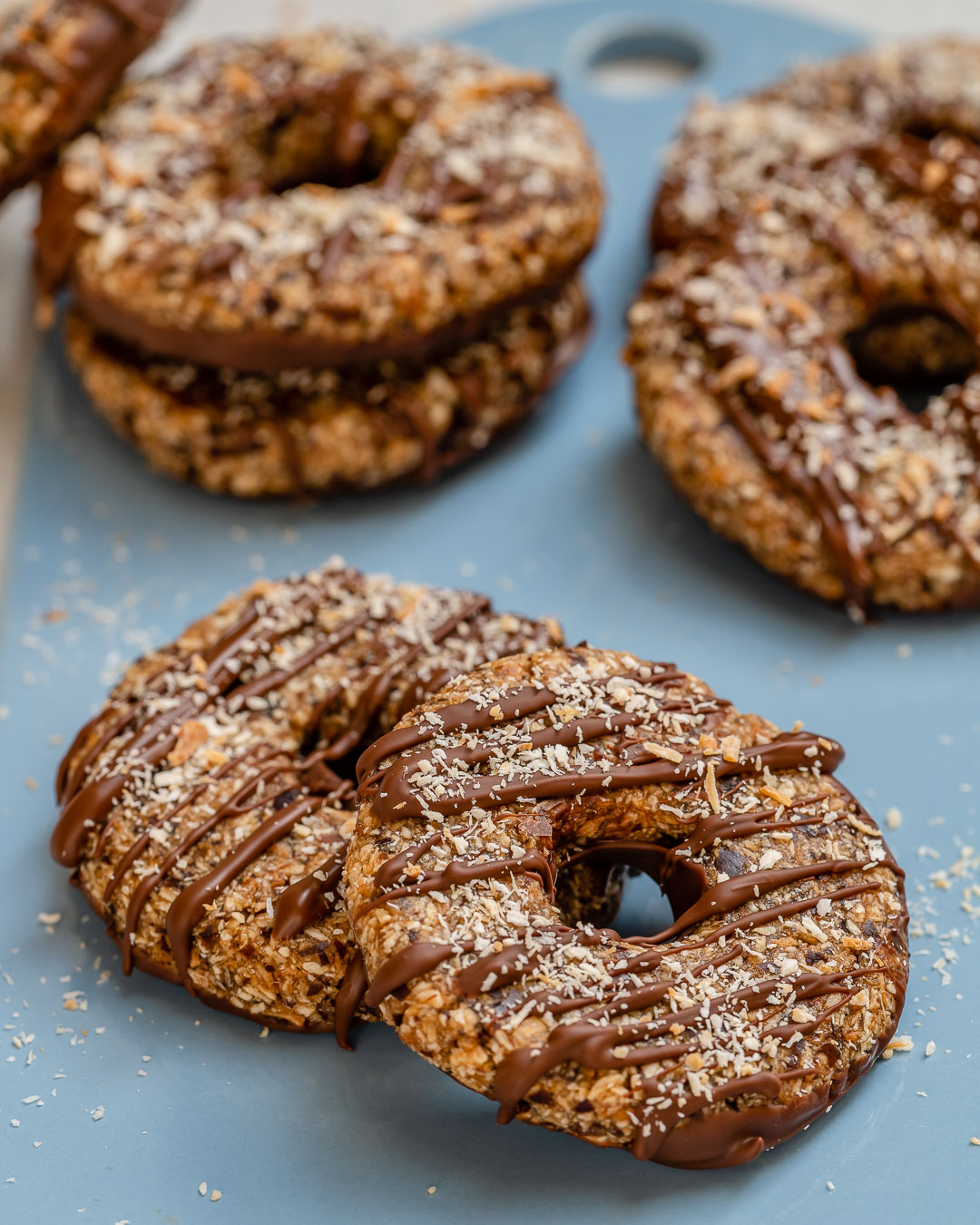 Chocolate drizzled, coconut sprinkled cookies laying on a blue background.