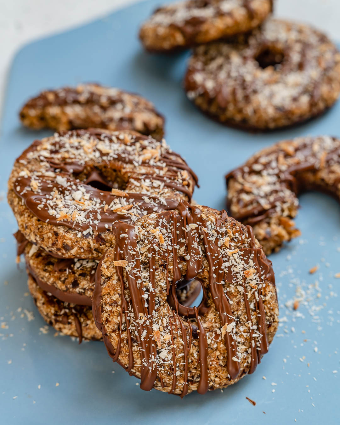 Image of samoa cookies drizzled with chocolate and sprinkled with toasted coconut, then stacked three high with one resting to the side of the stack.