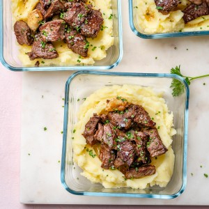Garlicy steak bites on top of mashed potatoes meal prepped into glass containers.