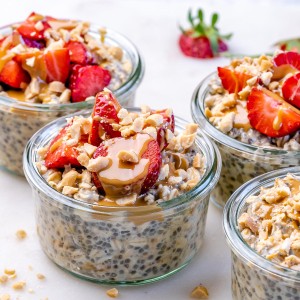 Four small jars of peanut butter overnight oats with strawberries and peanut butter drizzle on top.