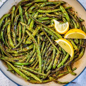 Seasoned seared green beans in a pan and garnished with lemon wedges.