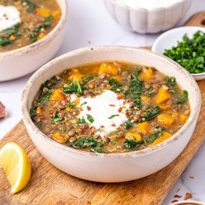 Butternut squash and green lentil soup topped with Greek yogurt and parsley flakes in a white bowl on a tan cutting board.