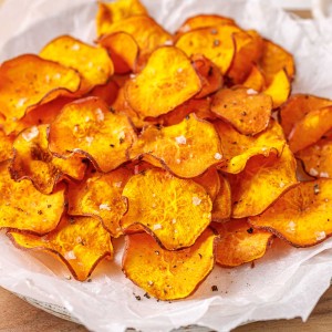 A pile of crispy air fryer sweet potato chips on parchment paper.
