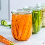Three clear glass jars; one with pickled carrots, one with pickled cucumbers, and one with pickled cauliflower.