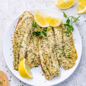 White fish made in the air fryer and served on a white plate garnished with lemon wedges and parsley.
