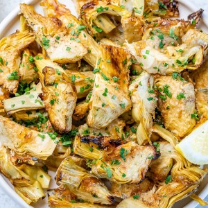 Roasted artichoke hearts with parmesan and no breadcrumbs on a plate and sprinkled with parsley flakes.
