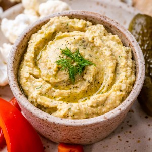 A grey speckled bowl filled with dill pickle hummus and garnished with fresh dill.