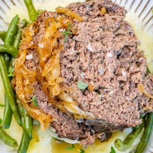 Two slices of French onion meatloaf on top of green beans on a white and blue plate.
