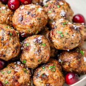 a white bowl of cranberry turkey meatballs garnished with parsley flakes and cranberries.