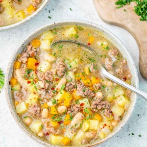 A spoon in a bowl of beef and bean soup that has been sprinkled with parsley flakes.