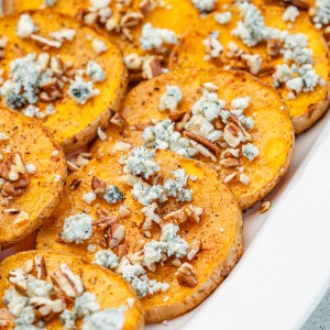 An appetizer platter filled with butternut squash slices that are tipped with blue cheese, chopped nuts, and a drizzle of honey.