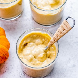 Creamy pumpkin pudding dessert in a glass jar with a tan spoon.