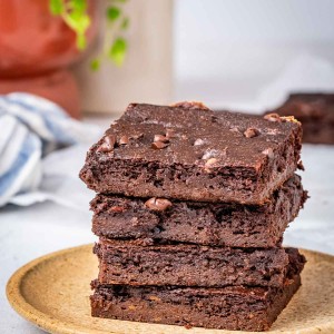 Four sweet potato brownies stacked on top of each other on a tan plate.