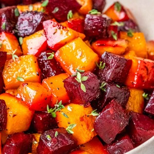 Roasted beets and butternut squash in a white bowl and garnished with herbs.