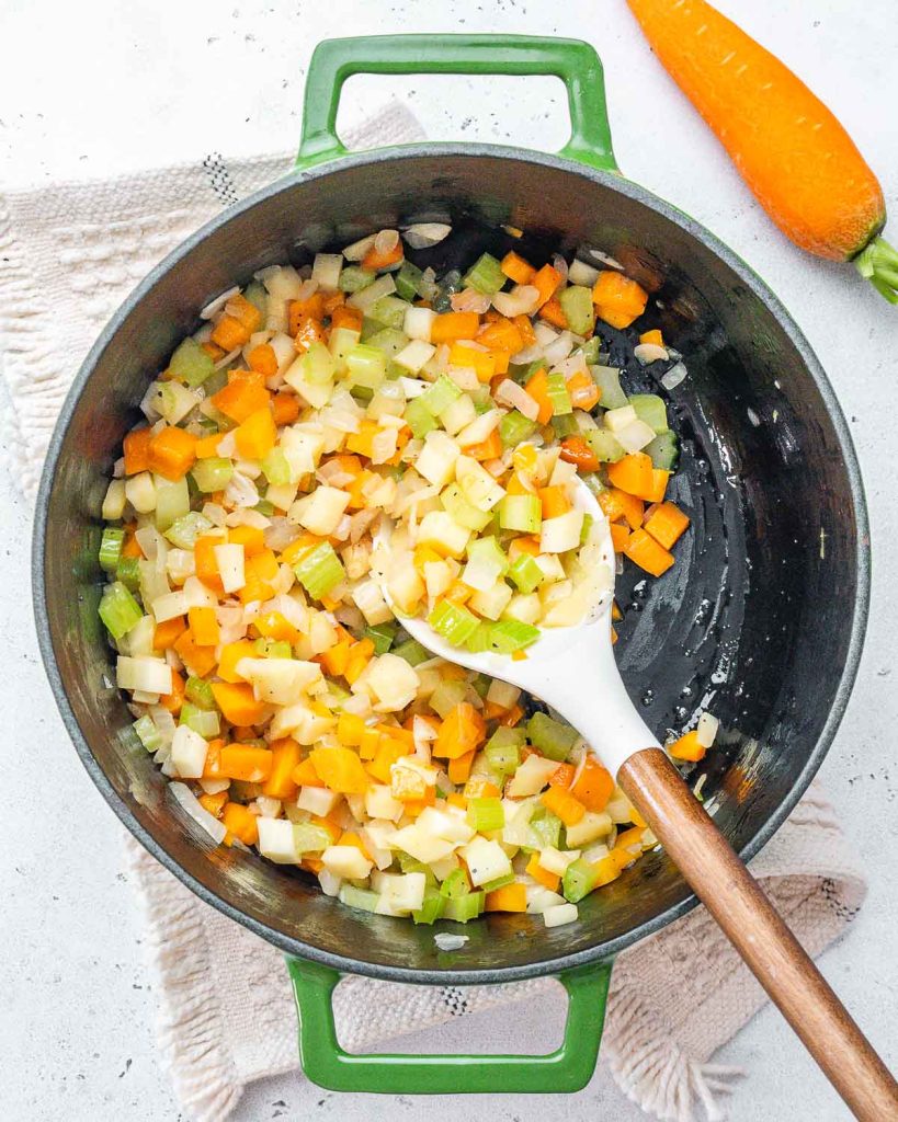 Chopped celery, parsnips, and carrots being sauteed in a large pot.