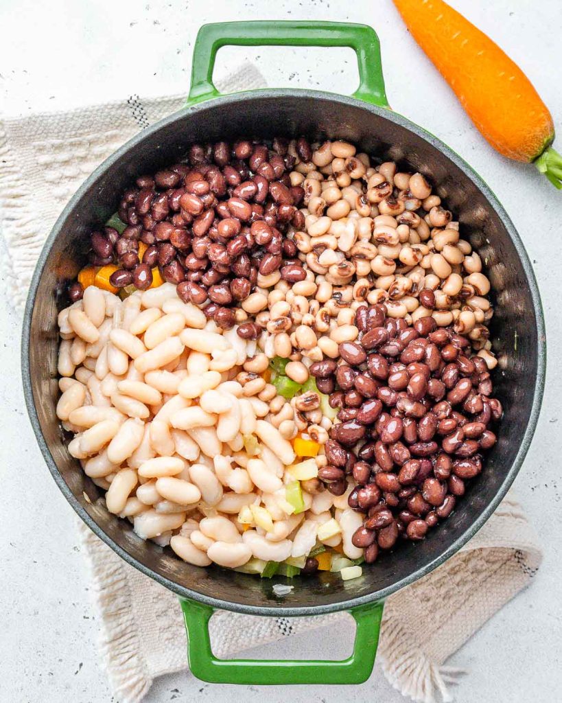Three kinds of beans being added to a pot with sauteed vegetables.