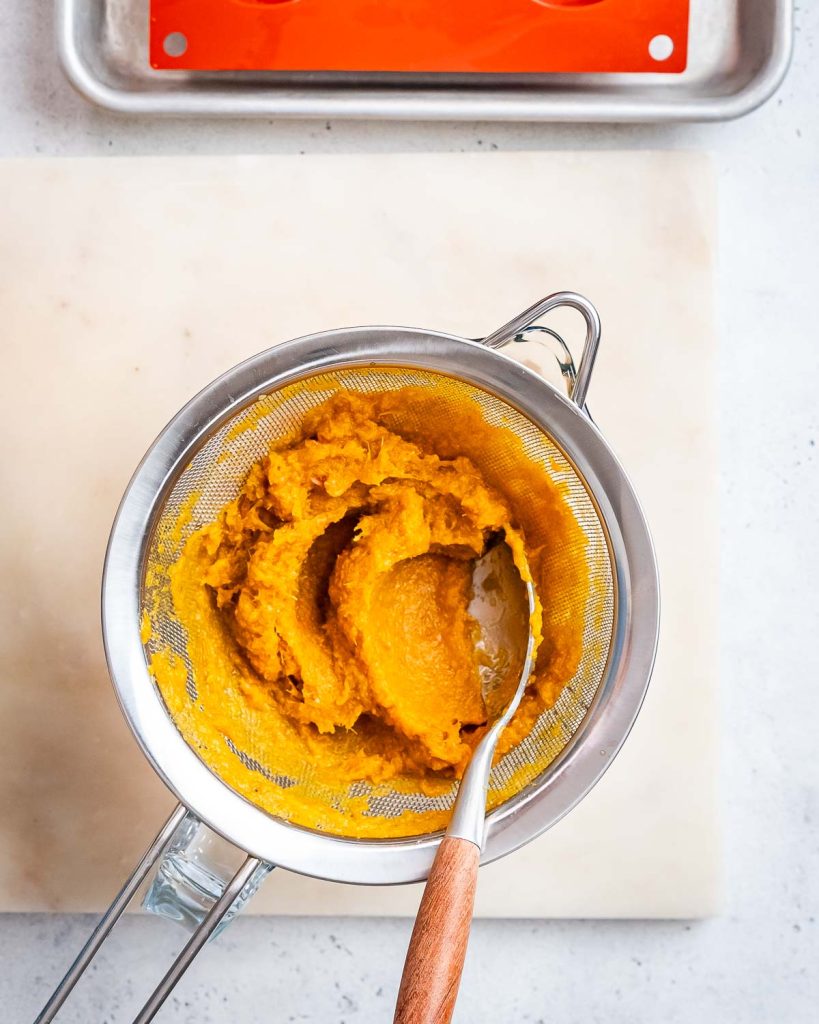 Orange puree being strained through a mesh strainer.