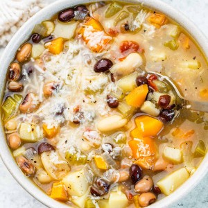 A hearty bowl of bean soup with three different types of bean, carrots, and onions, all topped with shredded parmesan cheese.