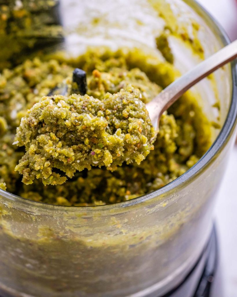 A spoonful of the green energy ball contents being taken out of the food processor.