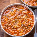 Bowl of unstuffed cabbage roll soup next to a silver spoon and set on a brown butcher block cutting board.