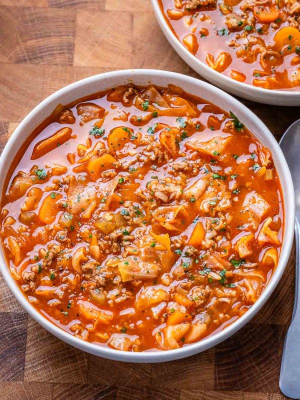 Bowl of unstuffed cabbage roll soup next to a silver spoon and set on a brown butcher block cutting board.
