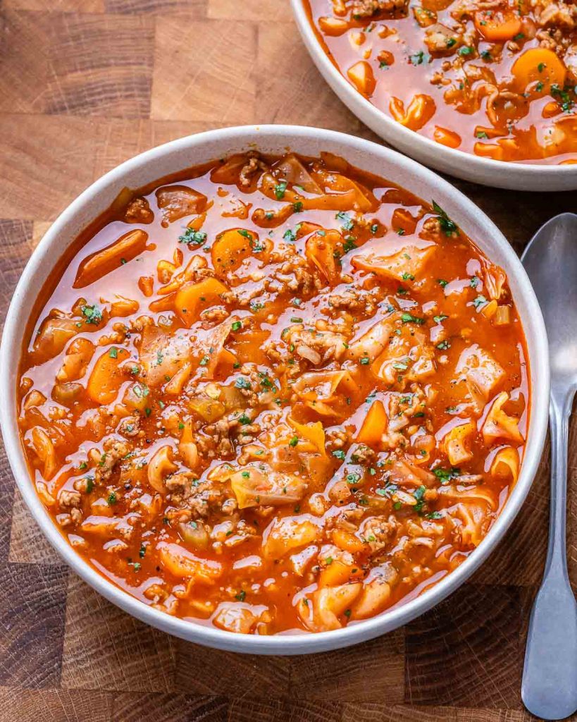 Bowl of unstuffed cabbage roll soup next to a silver spoon and set on a brown butcher block cutting board.