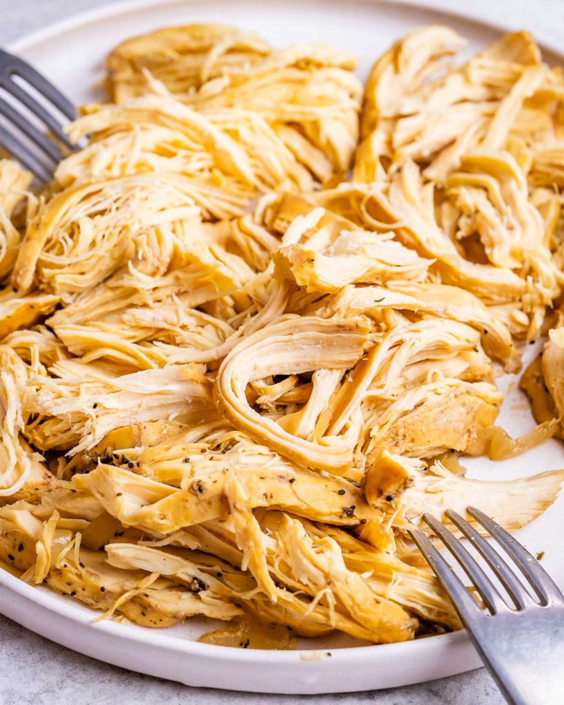 Cooked chicken from a slow cooker being shredded with a fork.