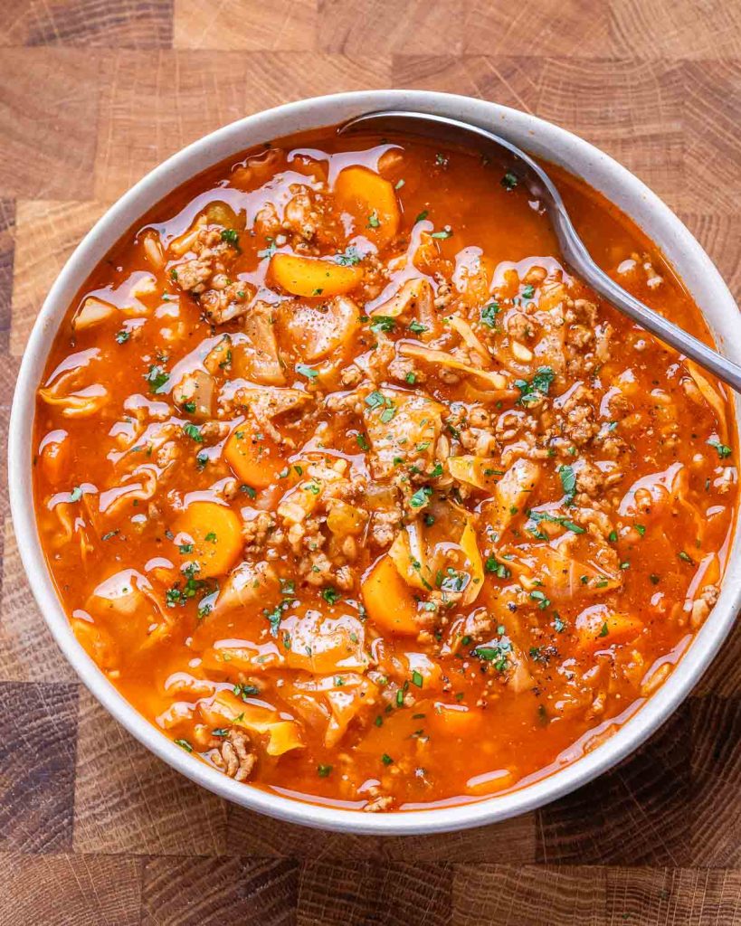Hearty, unstuffed cabbage roll soup in a bowl with a spoon on a brown butcher block background.