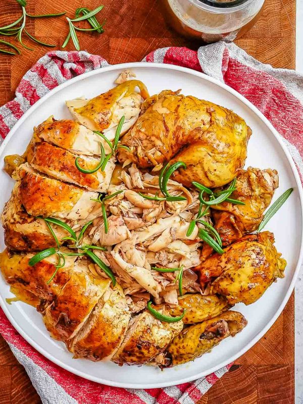 A whole balsamic baked chicken roasted and cut up into pieces and then plated on a white plate and garnished with green onions.