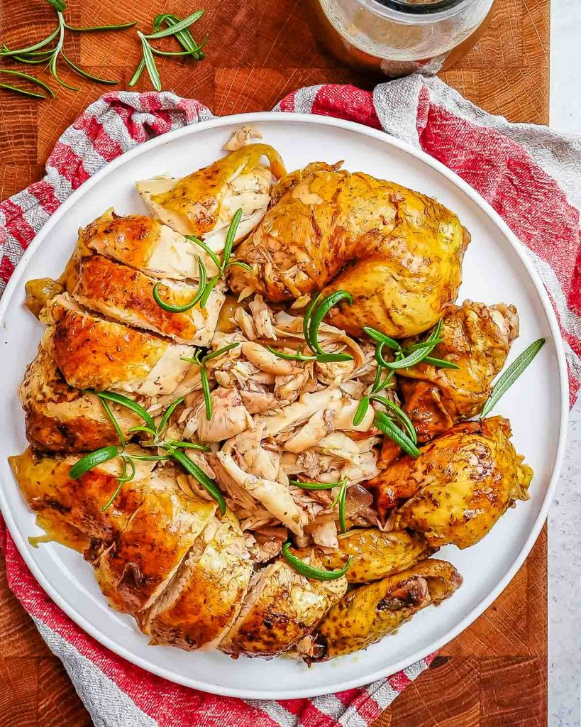A whole balsamic baked chicken roasted and cut up into pieces and then plated on a white plate and garnished with green onions.