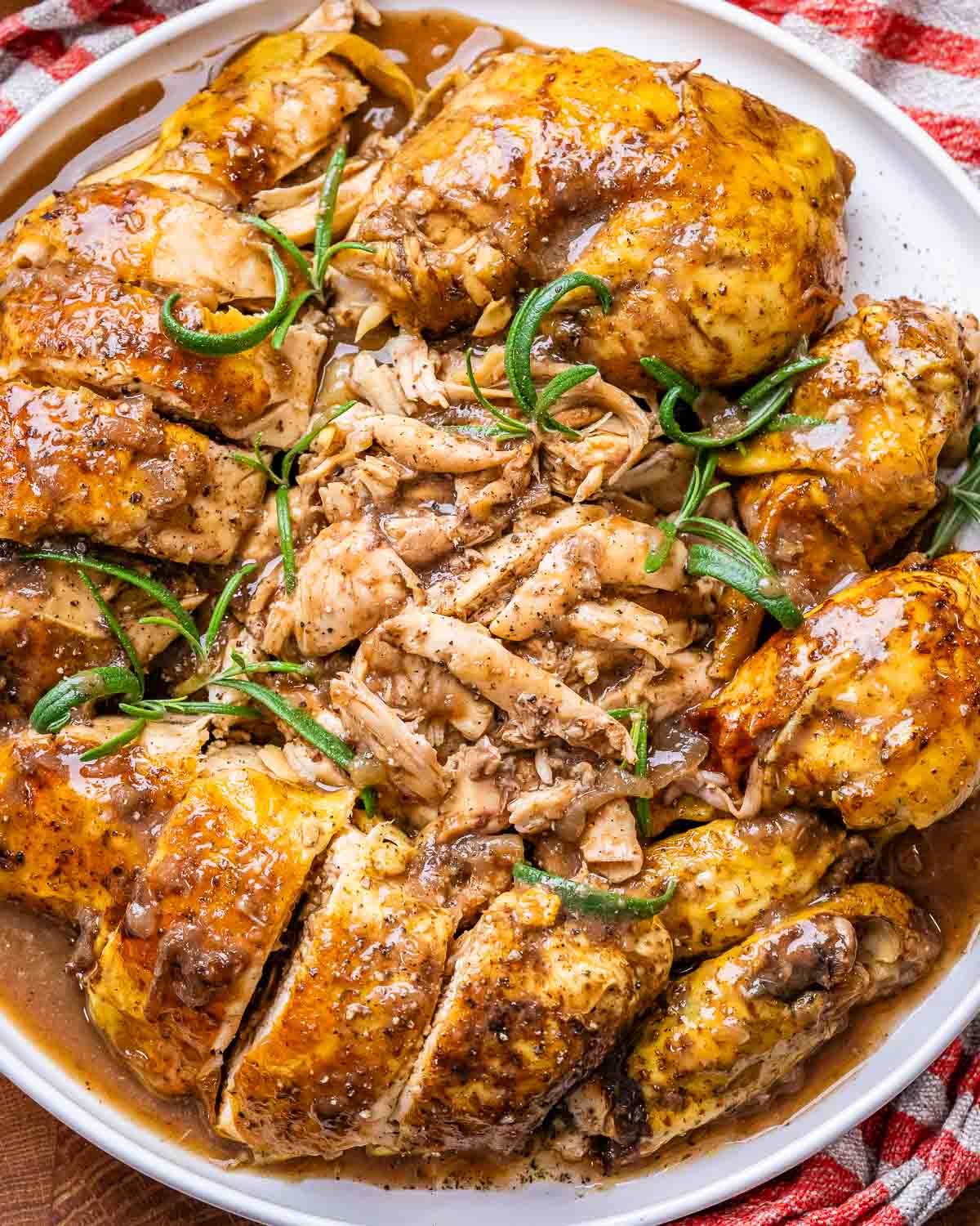 Pieces of balsamic chicken that have been sliced up and placed on a white plate, then sprinkled with pepper and sprigs of rosemary.