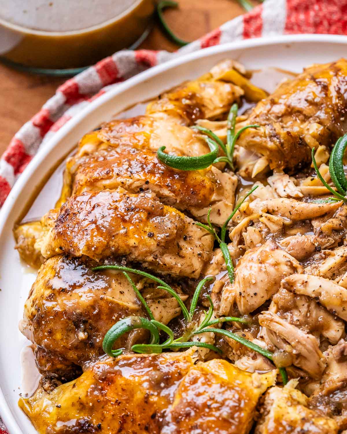 A close up of balsamic chicken on a white plate with rosemary after being baked.