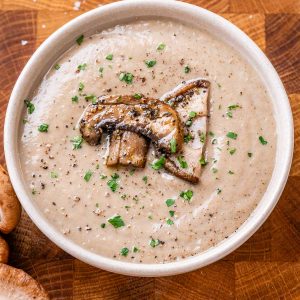 Creamy bowl of soup in a white bowl topped with two mushrooms and sprinkled with chopped parsley.
