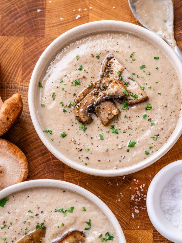 Two bowls of creamy mushroom soup topped with sliced mushrooms and parsley flakes.