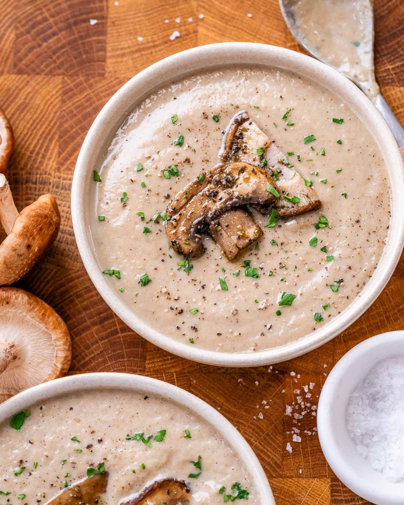 Two bowls of creamy mushroom soup topped with sliced mushrooms and parsley flakes.