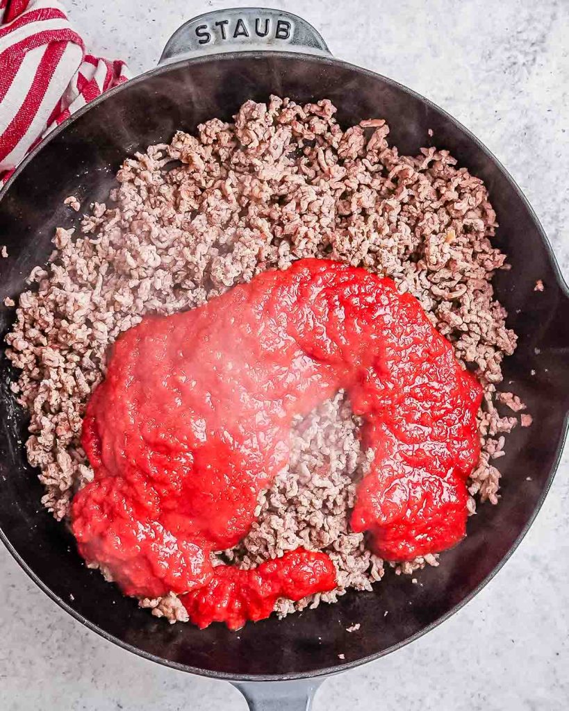 Cooked ground beef in a black skillet with red marinara sauce added to it.