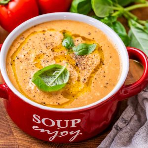 High-protein roasted tomato soup in a red bowl with a handle that says soup enjoy on the side in white letters.