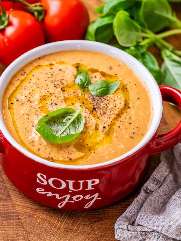 High-protein roasted tomato soup in a red bowl with a handle that says soup enjoy on the side in white letters.