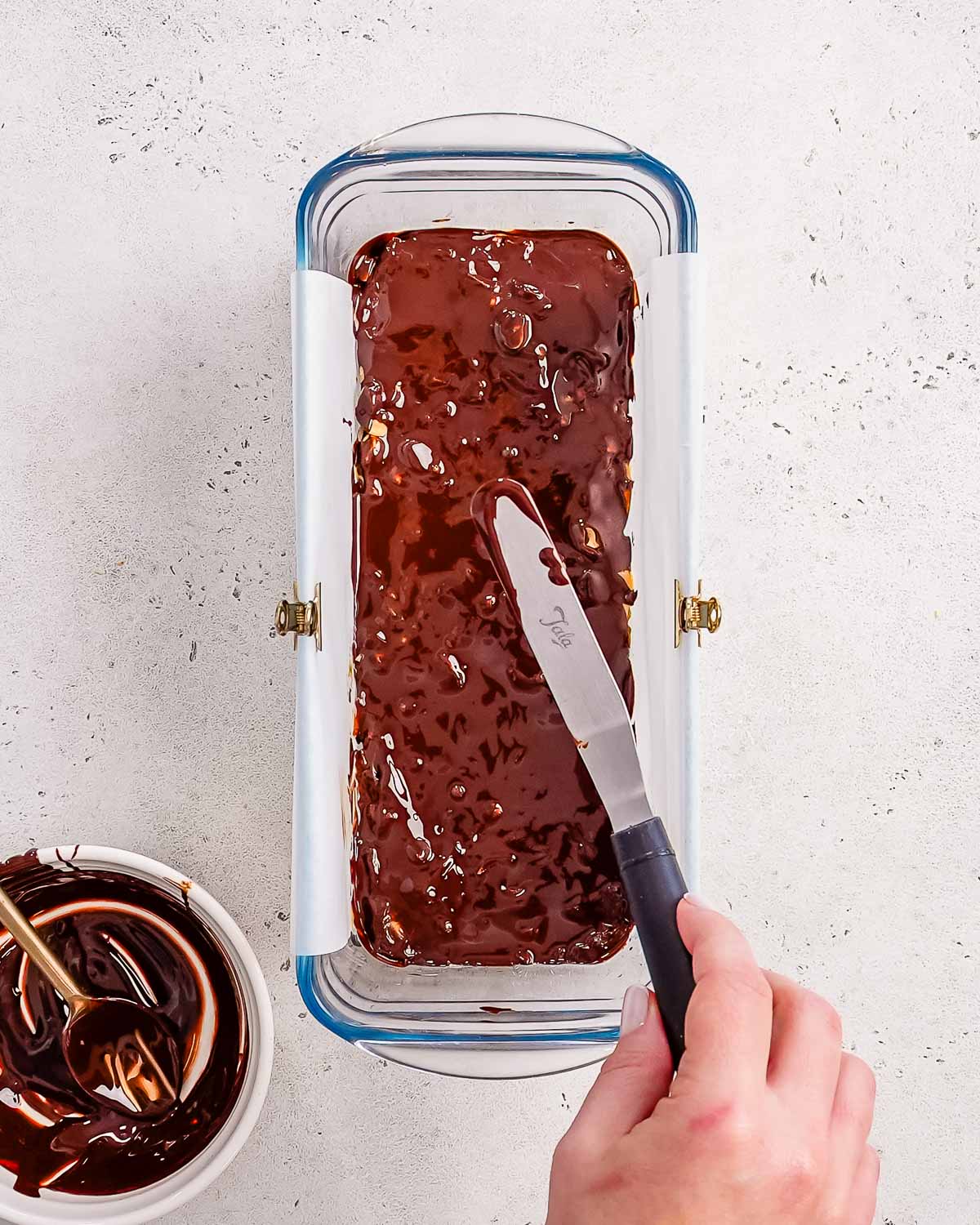 melted dark chocolate being spread over the top of the healthy date snickers bars.