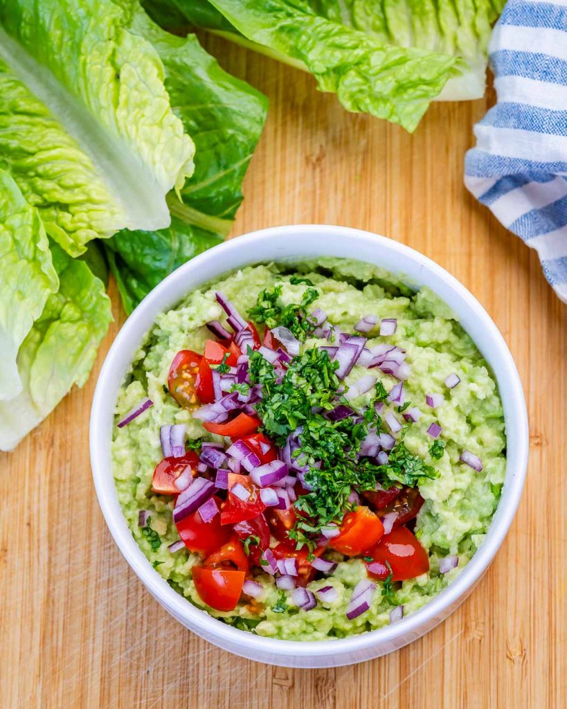 mashed avocado in a bowl with red onion, tomatoes and cilantro to make guacamole.