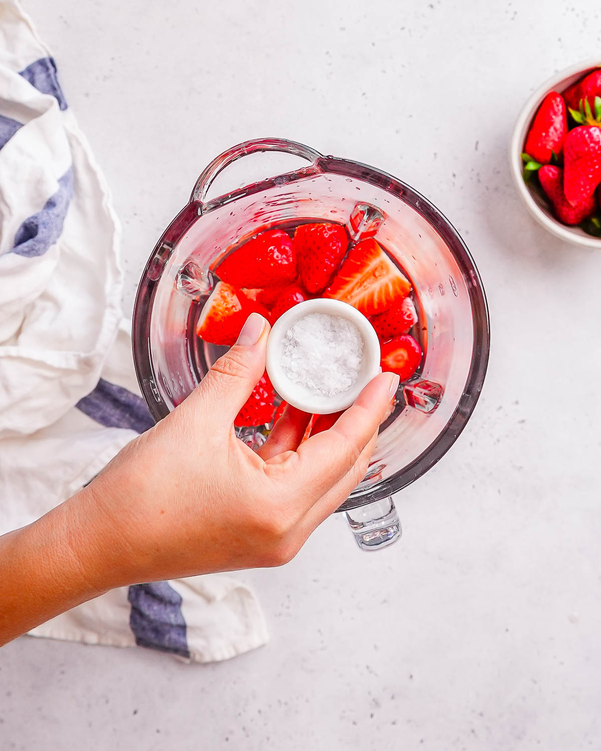 salt being added to blender with strawberries for electrolytes.