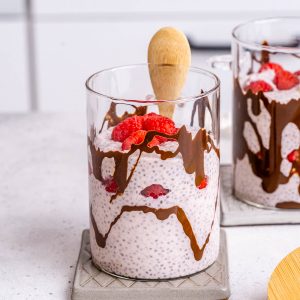 Protein chia pudding with lemon, raspberry, and chocolate in a small cup with a wooden spoon.