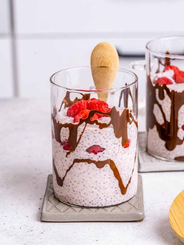 Protein chia pudding with lemon, raspberry, and chocolate in a small cup with a wooden spoon.