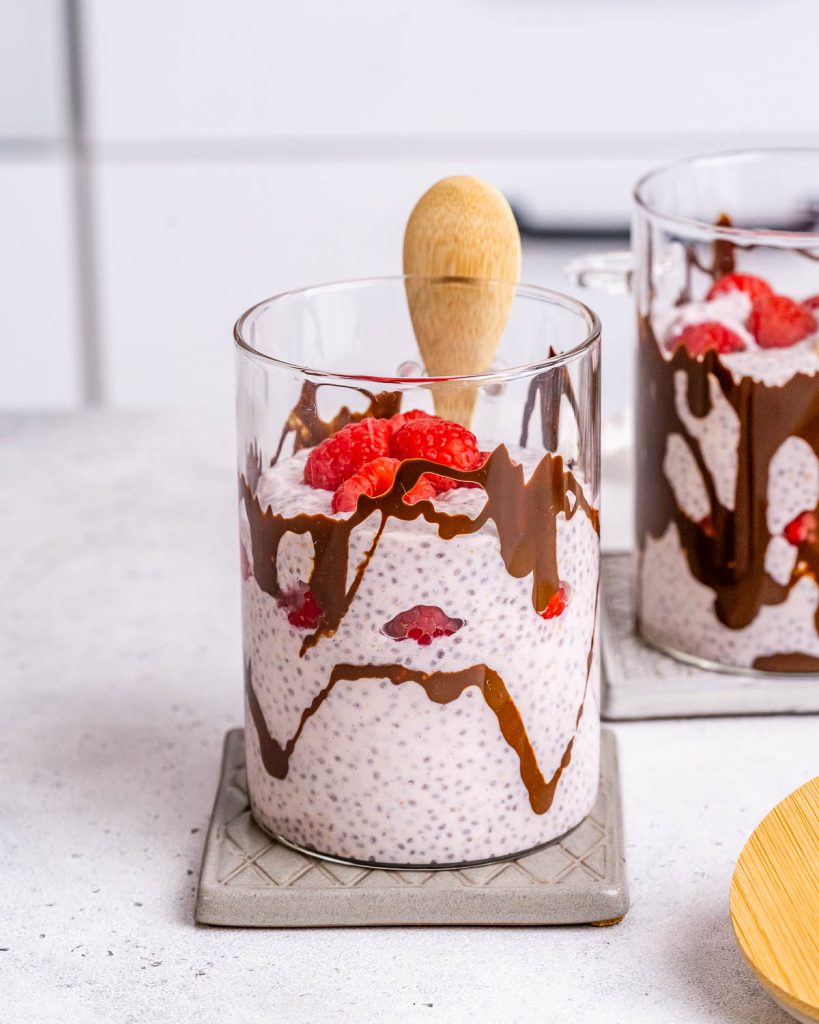 Protein chia pudding with lemon, raspberry, and chocolate in a small cup with a wooden spoon.